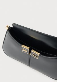 Μαύρη δερμάτινη τσάντα χειρός με λεία υφή, χρυσό κούμπωμα με δύο γεωμετρικά σχέδια και ευρύχωρο εσωτερικό.