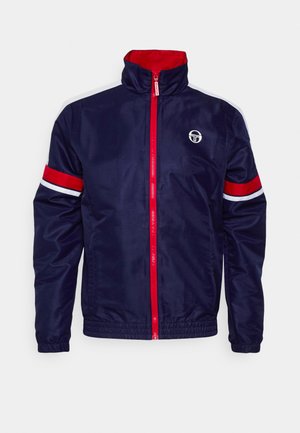 Mornarska jakna s windbreaker stilom, s visokim ovratnikom, crvenim patentnim zatvaračem i kontrastnim crvenim i bijelim prugastim naglascima na rukavima. Sadrži logo na prsima.