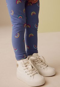 Collants bleus avec imprimés arc-en-ciel colorés, associés à des baskets montantes blanches avec une finition en toile texturée et un design à lacets.