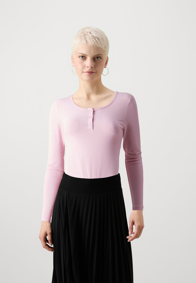 Langærmet pink bomuldsbluse med en rund udskæring og tre knaplukninger, parret med en sort plisseret nederdel med en strækbare talje.