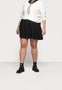 Suéter blanco de punto con un cuello negro y cordón negro, combinado con una falda negra acampanada y botas negras de tobillo con suelas gruesas.