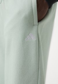 Joggers verdes menta feitos de tecido texturizado apresentam bolsos laterais e um logo prateado da Adidas na coxa esquerda.