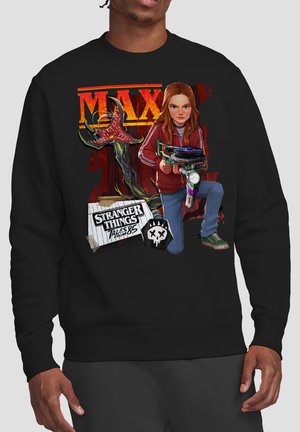 Junges Mädchen in roter Jacke, das eine Sci-Fi-Waffe anvisiert, mit einem Demogorgon und dem Schriftzug „Stranger Things Tales from '85“ auf einem schwarzen Sweatshirt.
