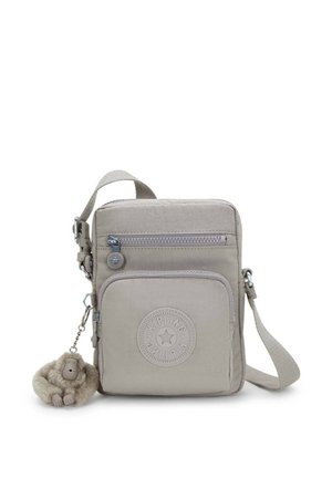 Beige crossbody taske lavet af letvægtsstof, med en lynlåslomme, cirkulært logo og en blød abe-nøglering fastgjort.