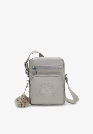 Beige crossbodytas gemaakt van lichtgewicht stof, met een ritssluiting, een rond logo en een pluchen apensleutelhanger eraan bevestigd.