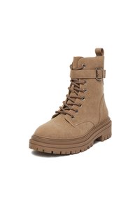 Karmelowe zamszowe botki za kostkę z zaokrąglonym noskiem, metalowymi oczkami, sznurowaniem na przodzie, regulowanym paskiem z klamrą oraz grubą, teksturowaną gumową podeszwą.