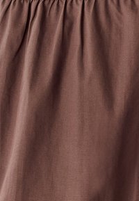 Rjavo blago z gladko teksturo in mehkim visečim. Material prikazuje subtilne variacije, kar ustvarja nežen, sproščen videz.