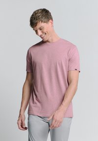 Lichtroze T-shirt met ronde hals, gemaakt van een zachte stof. Korte mouwen, ontspannen pasvorm, met een klein logo-accent op de linkermouw.