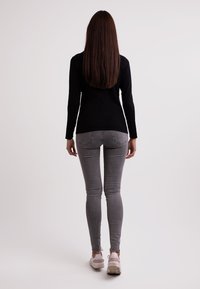 Svart långärmad topp, grå åtsittande jeans och vita sneakers. Rakt hår, sett från ryggen mot en ljus bakgrund.