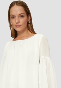 Witte blouse met lange, opgeblazen mouwen en een ronde halslijn. De stof lijkt licht en enigszins doorschijnend, wat bijdraagt aan een vloeiende silhouet.