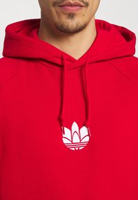 Rode hoodie met een trekkoord en geribde manchetten, voorzien van een wit geborduurd logo in het midden van de borst. Soepele katoenstof.