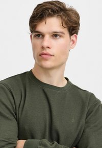 Olivengrøn crewneck sweatshirt lavet af et tekstureret, ribbet stof. Har lange ærmer og et subtilt logo på brystet.
