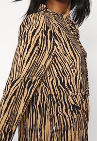 Eläinkuosilla varustettu mekko, jossa on mustia ja beigen raitoja, frillatut kaula-aukkot sekä pehmeä kangas. Mekossa on lentävä siluetti ja hienovaraisia valkoisia yksityiskohtia.