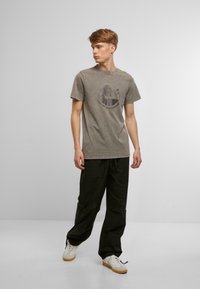 T-shirt en coton gris avec un col rond et des manches courtes, arborant un motif graphique d'un palmier, associé à un pantalon baggy noir.