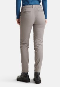 Personne portant un pantalon slim gris clair, des bottes noires à lacets et un haut à manches longues bleu, se tenant avec les mains détendues sur les côtés.