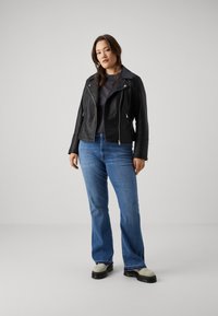 Black leather biker jacket with silver zipper, paired with blue flared jeans and chunky gray and black shoes. Simple, tailored fit.