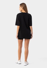 Melna pārsvītrota t-krekls ar īsām piedurknēm, izgatavots no kokvilnas auduma, ar brīvu piegriezumu. Nēsāts ar melniem šortiem un baltām sporta apaviem.