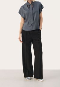 Blusa gris de manga corta con cuello con lazo y detalle de ojo de cerradura combinada con pantalones negros de pierna ancha y zapatos planos plateados.