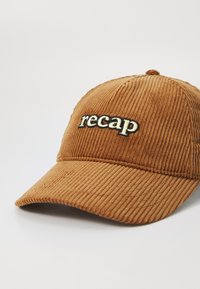 Hnědá kordurová čepice s prohnutým špichem a vyšitým textem "recap" v krémové a černé barvě. Materiál má po celé ploše drsnou texturu.