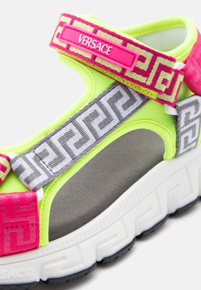 Νεον πράσινο και ροζ σανδάλι Versace με ρυθμιζόμενους λουρίδες με σχέδια και επενδυμένη σόλα σε λευκό φόντο.