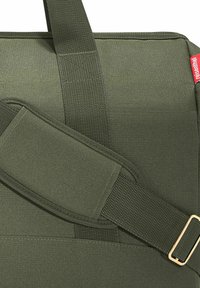 Sac en tissu vert avec des sangles en nylon robustes, une surface texturée et des accessoires en métal doré. Design compact et rectangulaire.