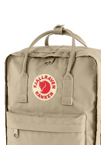 Sac à dos Fjällräven Kånken beige en tissu durable, avec un patch logo rond, deux sangles avant et une poche avant zippée.