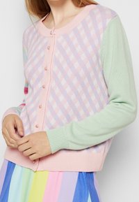 Pastellfärgad kofta med ett ljusrosa och lavendelfärgat diamantmönster, myntgröna ärmar och rosa knappar, tillverkad av mjukt stickat material.