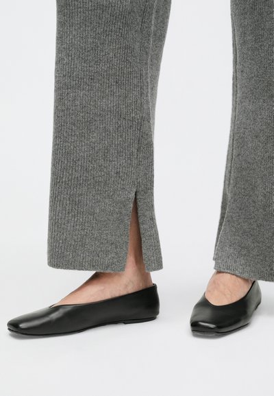 Sivé pruhované nohavice s bočnými rozparkami na leme, doplnené čiernymi koženými balerínkami s elegantným špicatým tvarom.