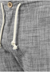Grå linneshorts med ett texturerat mönster, med en träknapp som stängning och krämfärgade snoddar. Närbild av tyg och design detaljer.