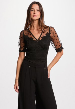 Zwarte blouse met doorzichtige puffmouwen met stippen en ingewikkelde kanten details, gecombineerd met hoge taille zwarte wijde broek.