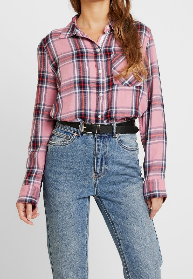 Rutig skjorta i rosa och blått med lång ärm, med en bröstficka, bärs tillsammans med högmidjade blå jeans och ett svart bälte.