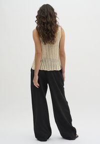 Lichtbeige geribde gebreide tanktop met open structuur, gecombineerd met losse, zwarte wijde broek met een relaxte, vloeiende silhouet.