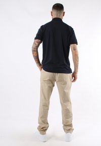 Polo navy de manga corta, combinado con chinos beiges y zapatillas blancas, mostrando tatuajes visibles en los brazos.