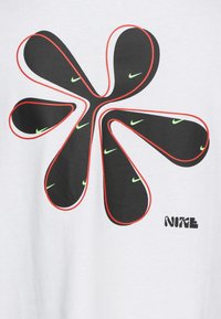 Vit t-shirt med en stor svart och röd grafisk design som liknar en blomma med gröna Nike-logotyper och blockbokstäver.
