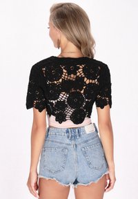 Top corto in cotone nero all'uncinetto con motivo floreale e maniche corte, abbinato a pantaloni corti di jeans blu chiaro a vita alta con orli sfrangiati.