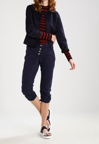 Námořnické zkrácené kalhoty s pomačkanou strukturou, spárované s námořnickou a červenou pruhovanou dlouhým rukávem. Sandály mají široký pásek a hladkou podrážku.