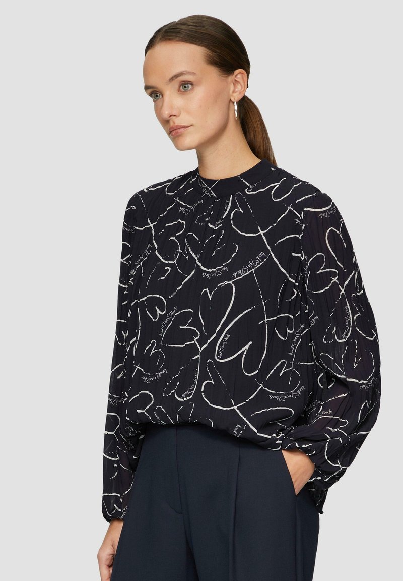 Blusa nera con stampa a cuore bianco e scritta, colletto alto, maniche plissettate e vestibilità rilassata. Tessuto morbido con una leggera texture.