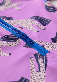 Tissu rose avec un motif de cheval et des détails tachetés. Une fermeture éclair bleue est placée au centre, avec des coutures contrastantes et une texture lisse.