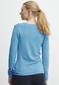 Pull à manches longues bleu clair en matière douce, avec un col rond, des poignets et un ourlet côtelés, et une coupe ajustée.