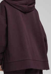 Felpa oversized viola in tessuto strutturato, dotata di cappuccio con cordino e spacchi laterali all'orlo per un maggiore comfort e libertà di movimento.