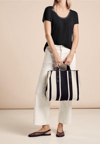 Svart kortärmad topp, vita vida byxor, randig väska i svart och krämfärgad med dubbla handtag, samt svarta mesh-sandaler.