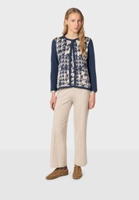 Knit cardigan with navy sleeves and a cream patterned front, paired with beige wide-leg trousers and brown sneakers. Simple design.