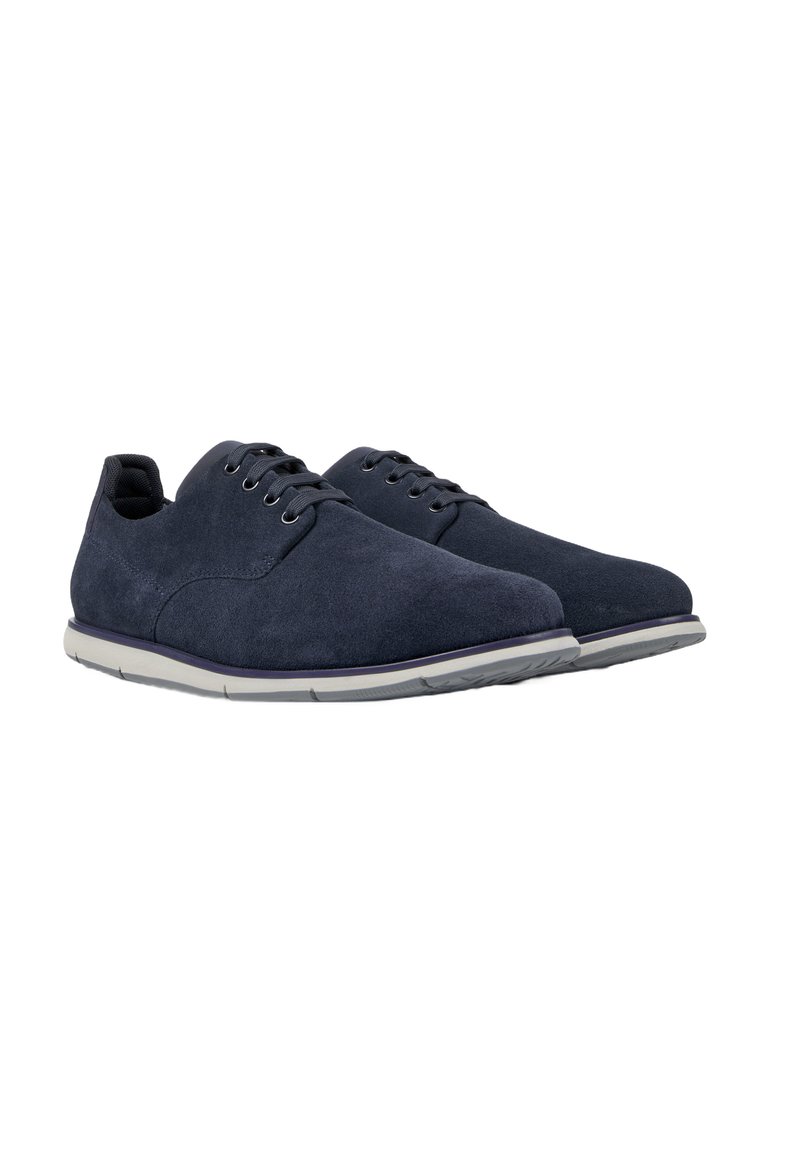 Marineblauwe suède schoenen met een lage ontwerp, voorzien van zes oogjes, grijze zolen en een gladde textuur. De veters zijn in dezelfde marineblauwe kleur.