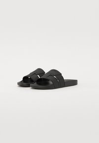 Infradito in gomma nera con due ampi cinturini caratterizzati da un design texturizzato e un logo. Punta aperta con suole piatte per un look casual.