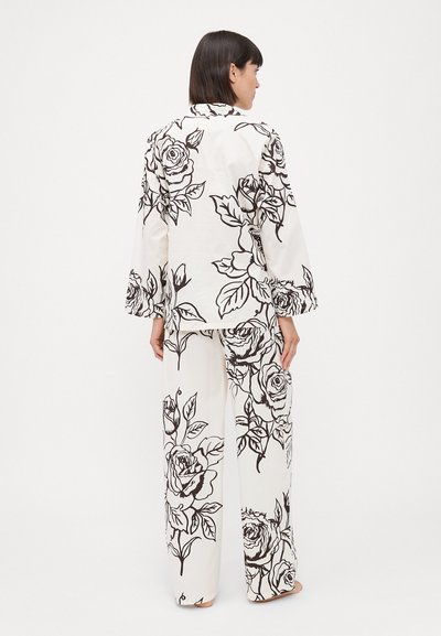 Set de loungewear cu imprimeu floral, având un fundal alb cu modele de trandafiri negri, mâneci lungi și pantaloni lejeri.