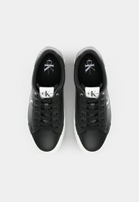 Zapatillas negras de cuero, con suelas de goma blanca, punta redonda y un detalle de logo en el lado. Diseño de cordones con cordones planos.