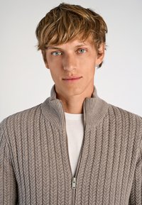 Kardigan med dragkedja i ljusgrå ribbad stickning, med ståkrage och diskret dragkedja. Mjuk textur och strukturerad design.