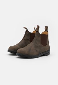 Bottes chelsea en cuir marron avec panneaux élastiques sur les côtés, bout rond et languettes de tirage. Tige texturée et semelle en caoutchouc noir pour une meilleure adhérence.