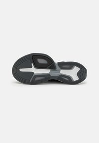 Schwarze und weiße Sneaker-Sohle mit strukturiertem Griff und sichtbarem "TORSION SYSTEM"-Label im Mittelfußbereich vor einem schlichten Hintergrund.