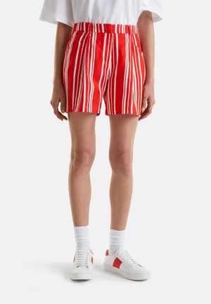 Pantalones cortos a rayas verticales rojas y blancas, usados con calcetines blancos y zapatillas blancas con detalles rojos en una persona parada frente a un fondo simple.